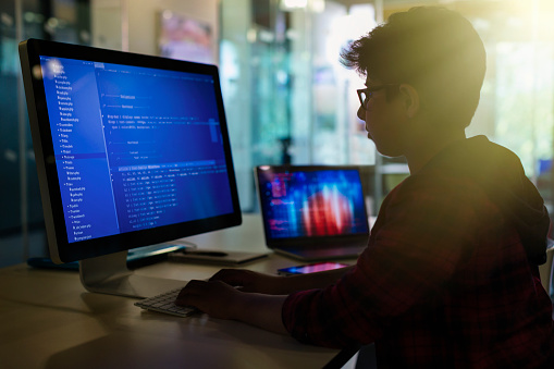 Boy student programming at computer in dark classroom